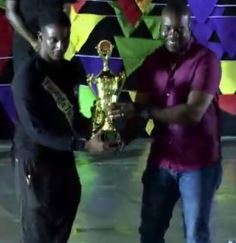 New Dimension band member  representative (at left) is presented with the 2019 Grenada National Panorama championship trophy