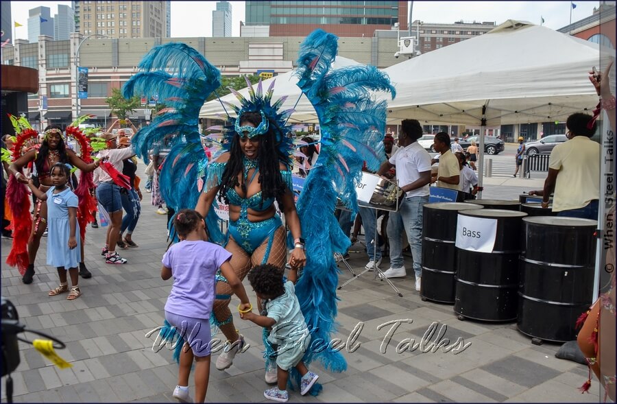 Children enjoy dancing with Sesame Flyers’ costumed masqueraders to the sounds of Eruption Steel Orchestra