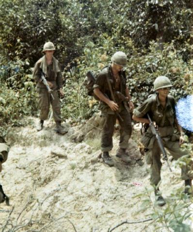 On patrol in Hobo Woods, troops walk past bomb crater in wake of bombing assault on VC