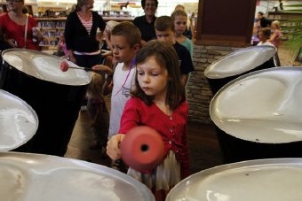 Keira Behnke, 7, of Grand Haven, center, uses a mallet to use of the bass steel drums after listening to Caribbean Island music from West Michigan steel drum band Steel Doin' It at the Loutit District Library on August 15, 2013